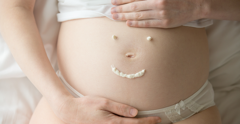 Schwangere Frau zeichnet Smiley auf Bauch